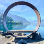 a circular sculpture sitting on top of a rock near a body of water